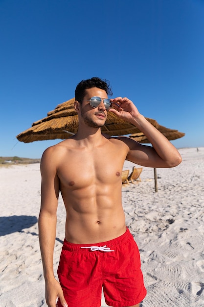 Foto homem caucasiano aproveitando o tempo na praia em um dia ensolarado, de pé e olhando para longe com o céu azul ao fundo