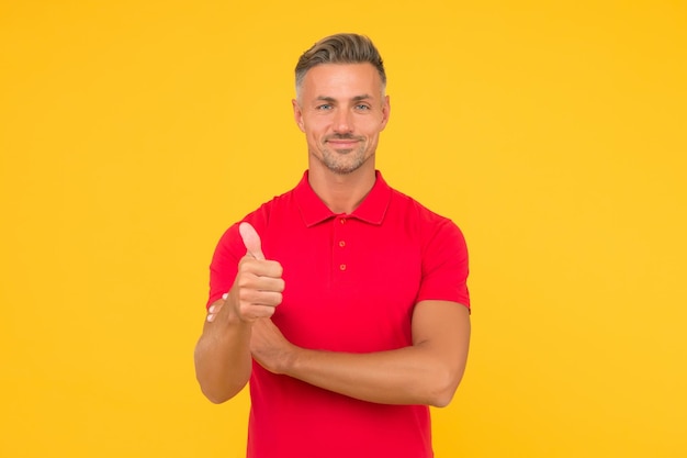 Homem caucasiano atraente usa camiseta vermelha em estilo casual mostrando polegares para cima gesto de aprovação com a mão fundo amarelo bonito