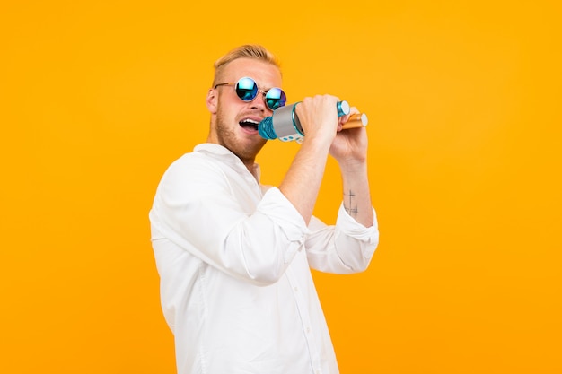 Homem caucasiano bonito com óculos canta músicas em karaoke com microfone isolado em amarelo