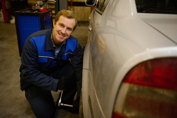 Foto homem caucasiano bonito, mecânico de automóveis profissional muda manualmente a roda do carro, desaparafusando as porcas e parafusos com a chave, sorrindo para a câmera na oficina. conceito de serviço automático