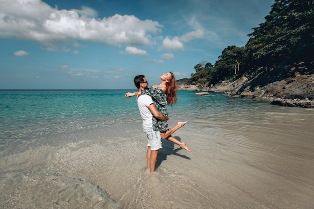 Homem caucasiano, carregando sua namorada ruiva, desfrutando de um final de tarde juntos na praia. Phuket. Tailândia.