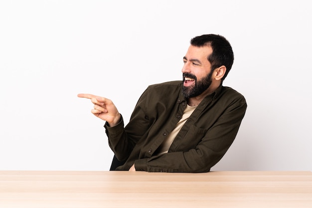 Homem caucasiano com barba em uma mesa, apontando o dedo para o lado e apresentando um produto.