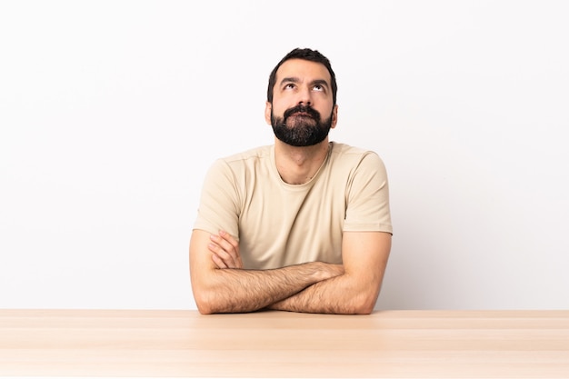 Homem caucasiano com barba em uma mesa e olhando para cima