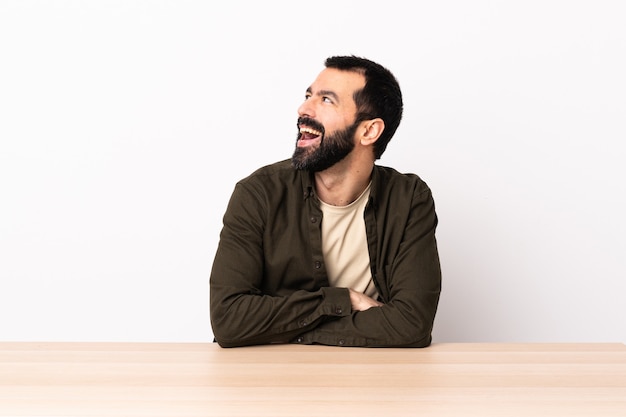 Homem caucasiano com barba em uma mesa feliz e sorridente.