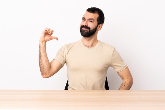 Homem caucasiano com barba em uma mesa orgulhosa e satisfeita.