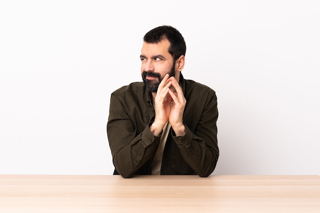 Homem caucasiano com barba em uma mesa, planejando algo.