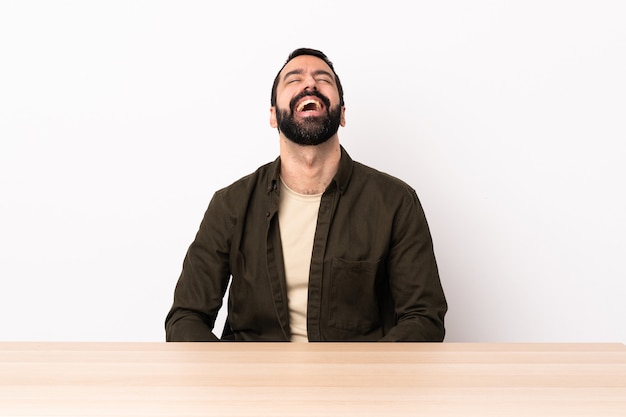 Homem caucasiano com barba em uma mesa rindo.