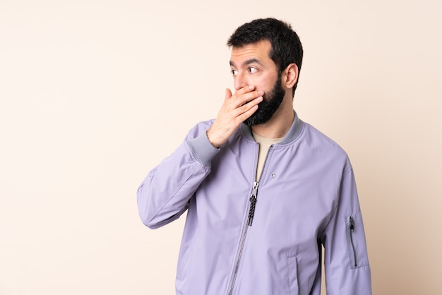 Homem caucasiano com barba, vestindo um casaco por cima da parede, fazendo o gesto de surpresa enquanto olha para o lado