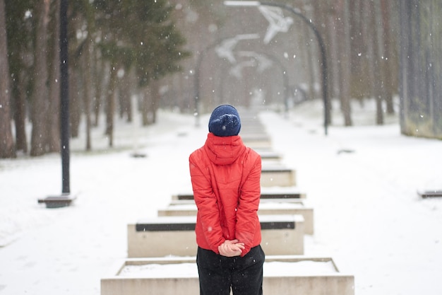 Homem caucasiano com jaqueta vermelha curtindo a queda de neve no parque, parado na frente
