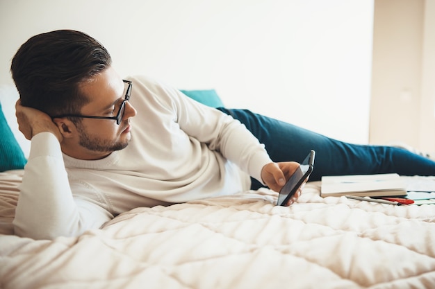 Homem caucasiano com óculos, deitado na cama e conversando ao telefone depois de fazer cursos online