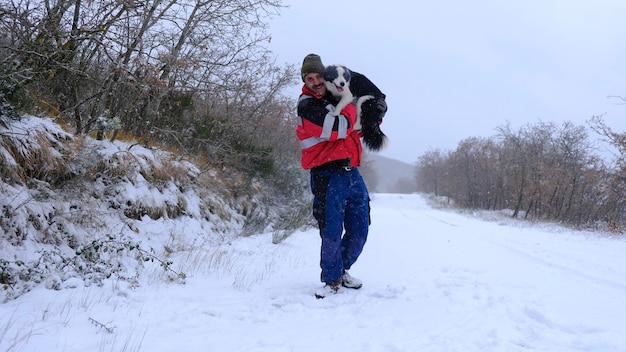 Homem caucasiano com um cachorro Border Collie em seus braços na neve