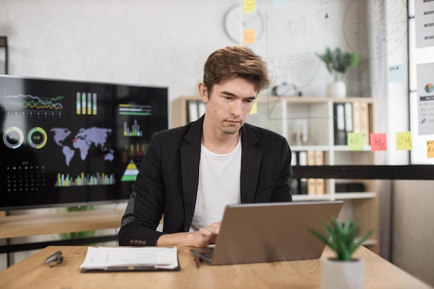 Homem caucasiano confiante em camisa branca sentado no escritório e usando laptop sem fio
