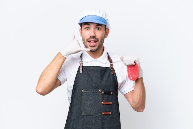 Homem caucasiano de açougueiro vestindo um avental e servindo carne fresca cortada sobre fundo branco isolado, fazendo gesto de telefone Ligue-me de volta sinal