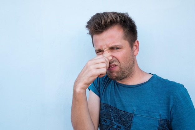 Homem caucasiano de camisa azul, fechando o nariz por causa do mau cheiro