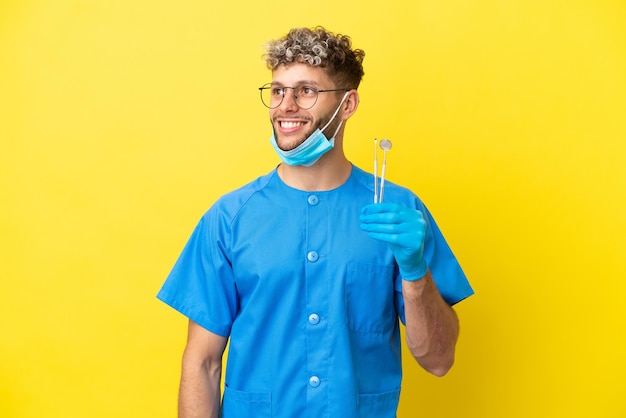 Homem caucasiano de dentista segurando ferramentas isoladas em um fundo amarelo, tendo uma ideia enquanto olha para cima