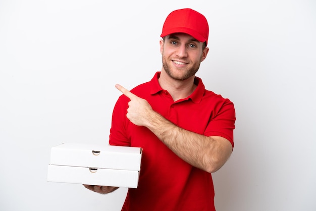 Homem caucasiano de entrega de pizza com uniforme de trabalho pegando caixas de pizza isoladas no fundo branco, apontando para o lado para apresentar um produto