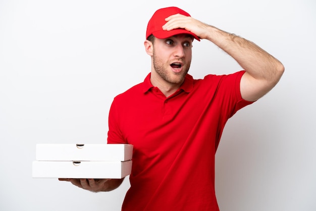 Homem caucasiano de entrega de pizza com uniforme de trabalho pegando caixas de pizza isoladas no fundo branco fazendo gesto de surpresa enquanto olha para o lado