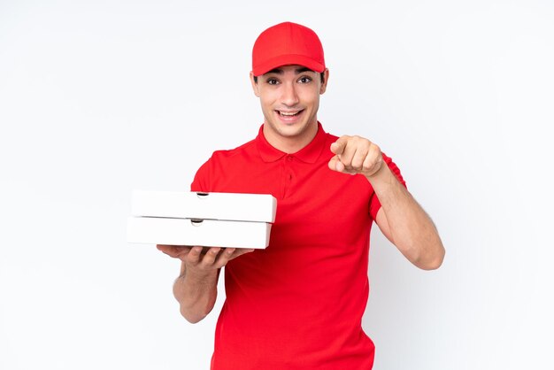 Homem caucasiano de entrega de pizza com uniforme de trabalho pegando caixas de pizza isoladas no fundo branco surpreso e apontando para a frente