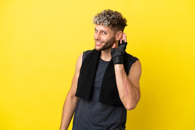 Homem caucasiano de esporte isolado em um fundo amarelo, ouvindo algo colocando a mão na orelha