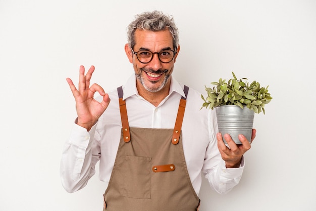 Homem caucasiano de jardineiro de meia idade segurando uma planta isolada no fundo branco alegre e confiante, mostrando o gesto okey