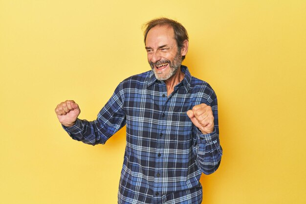 Foto homem caucasiano de meia idade em estúdio amarelo dançando e se divertindo