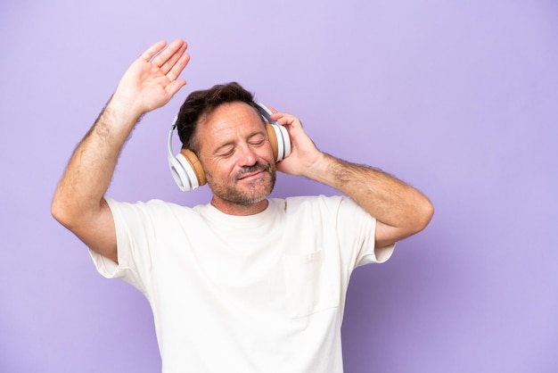 Homem caucasiano de meia-idade isolado em fundo roxo ouvindo música e dançando