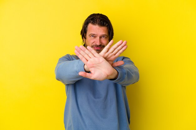 Homem caucasiano de meia-idade isolado na parede amarela fazendo um gesto de negação