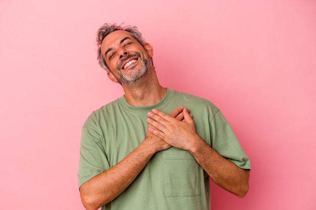 Homem caucasiano de meia-idade, isolado no fundo rosa, rindo, mantendo as mãos no coração, o conceito de felicidade.