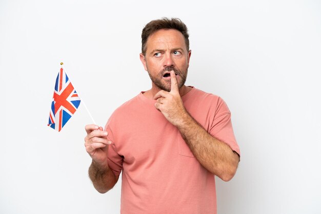 Homem caucasiano de meia-idade segurando a bandeira inglesa isolada no fundo branco tendo dúvidas enquanto olha para cima