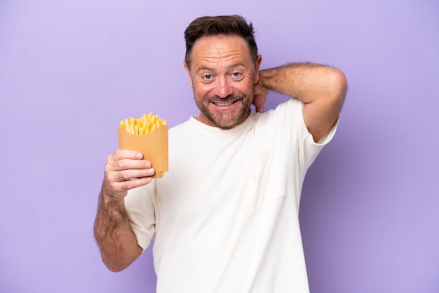 Homem caucasiano de meia-idade segurando batatas fritas isoladas em fundo roxo rindo