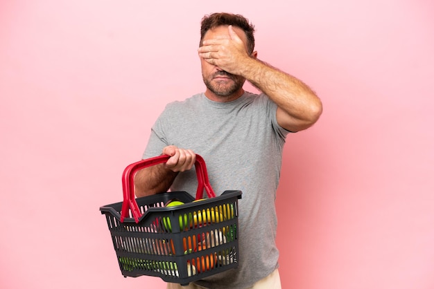 Homem caucasiano de meia-idade segurando uma cesta de compras isolada em fundo rosa