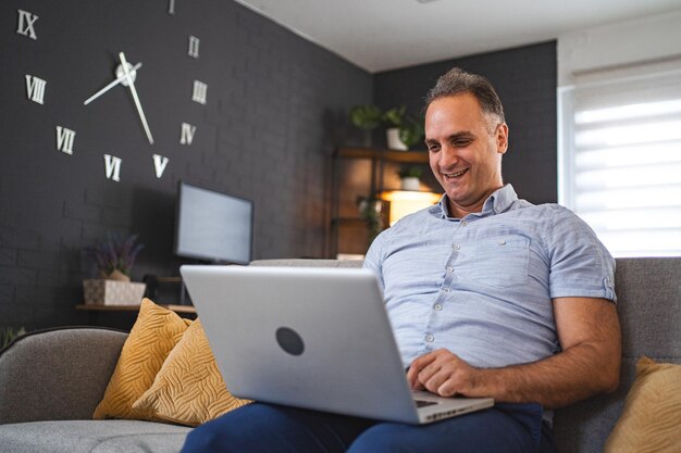 Homem caucasiano de meia-idade usando laptop no sofá