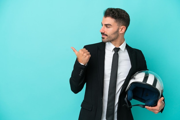 Homem caucasiano de negócios com capacete de moto isolado em fundo azul, apontando para o lado para apresentar um produto
