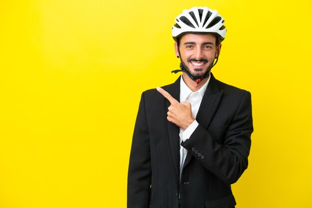 Homem caucasiano de negócios com um capacete de bicicleta isolado em fundo amarelo, apontando para o lado para apresentar um produto