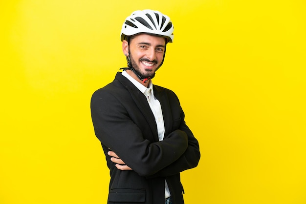 Homem caucasiano de negócios com um capacete de bicicleta isolado em fundo amarelo com braços cruzados e olhando para a frente