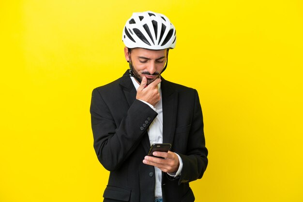 Homem caucasiano de negócios com um capacete de bicicleta isolado em fundo amarelo pensando e enviando uma mensagem