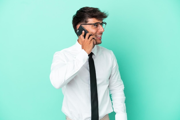 Homem caucasiano de negócios isolado em fundo azul, mantendo uma conversa com o celular com alguém