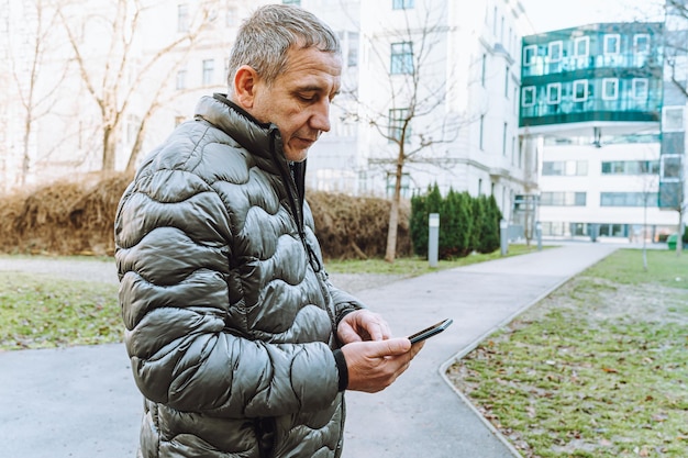 Homem caucasiano de quarenta anos olhando para o celular. Edifícios de rua e cidade como pano de fundo.