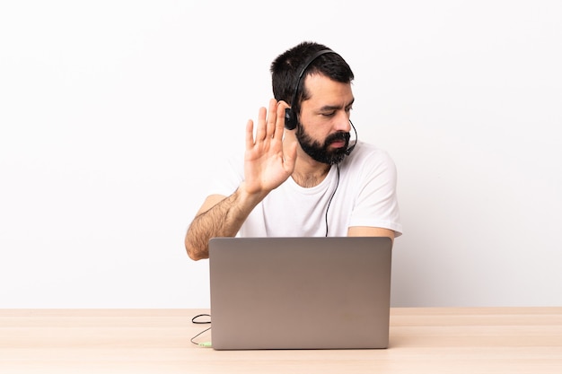 Homem caucasiano de telemarketing trabalhando com um fone de ouvido e com laptop fazendo gesto de pare e decepcionado.