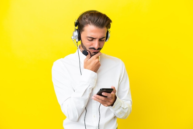 Homem caucasiano de telemarketing trabalhando com um fone de ouvido isolado em fundo amarelo pensando e enviando uma mensagem