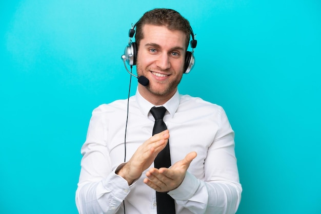 Homem caucasiano de telemarketing trabalhando com um fone de ouvido isolado em fundo azul aplaudindo após apresentação em uma conferência
