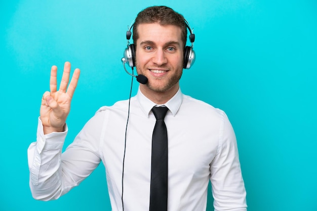 Homem caucasiano de telemarketing trabalhando com um fone de ouvido isolado em fundo azul feliz e contando três com os dedos