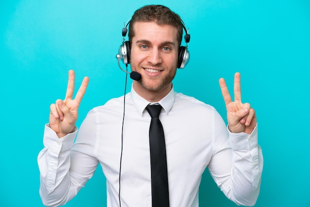 Homem caucasiano de telemarketing trabalhando com um fone de ouvido isolado em fundo azul, mostrando sinal de vitória com as duas mãos