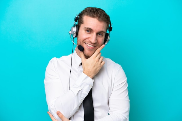 Homem caucasiano de telemarketing trabalhando com um fone de ouvido isolado em fundo azul sorrindo