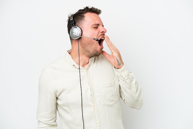 Homem caucasiano de telemarketing trabalhando com um fone de ouvido isolado no fundo branco, bocejando e cobrindo a boca aberta com a mão