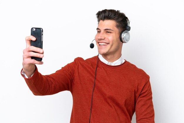 Homem caucasiano de telemarketing trabalhando com um fone de ouvido isolado no fundo branco, fazendo uma selfie