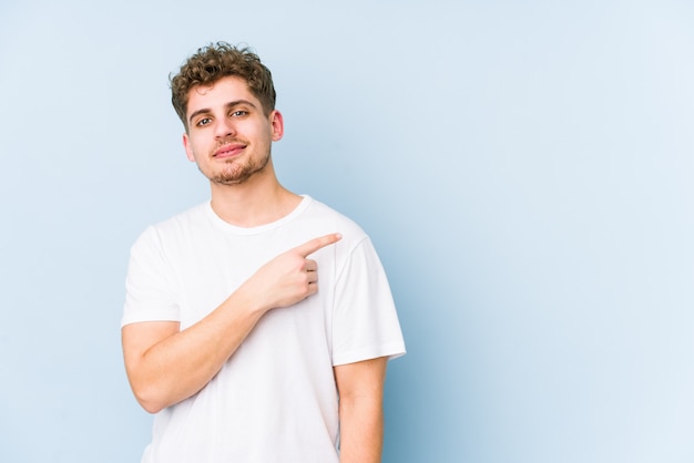 Homem caucasiano do cabelo encaracolado louro novo que sorri e que aponta de lado, mostrando algo no espaço em branco.