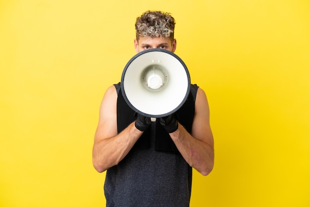 Homem caucasiano esportivo isolado em um fundo amarelo gritando em um megafone