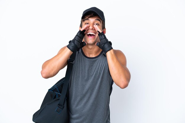 Homem caucasiano esportivo jovem com bolsa esportiva isolada em fundo branco gritando e anunciando algo