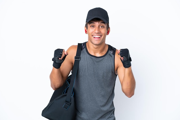 Homem caucasiano esportivo jovem com bolsa esportiva isolada no fundo branco comemorando uma vitória na posição de vencedor